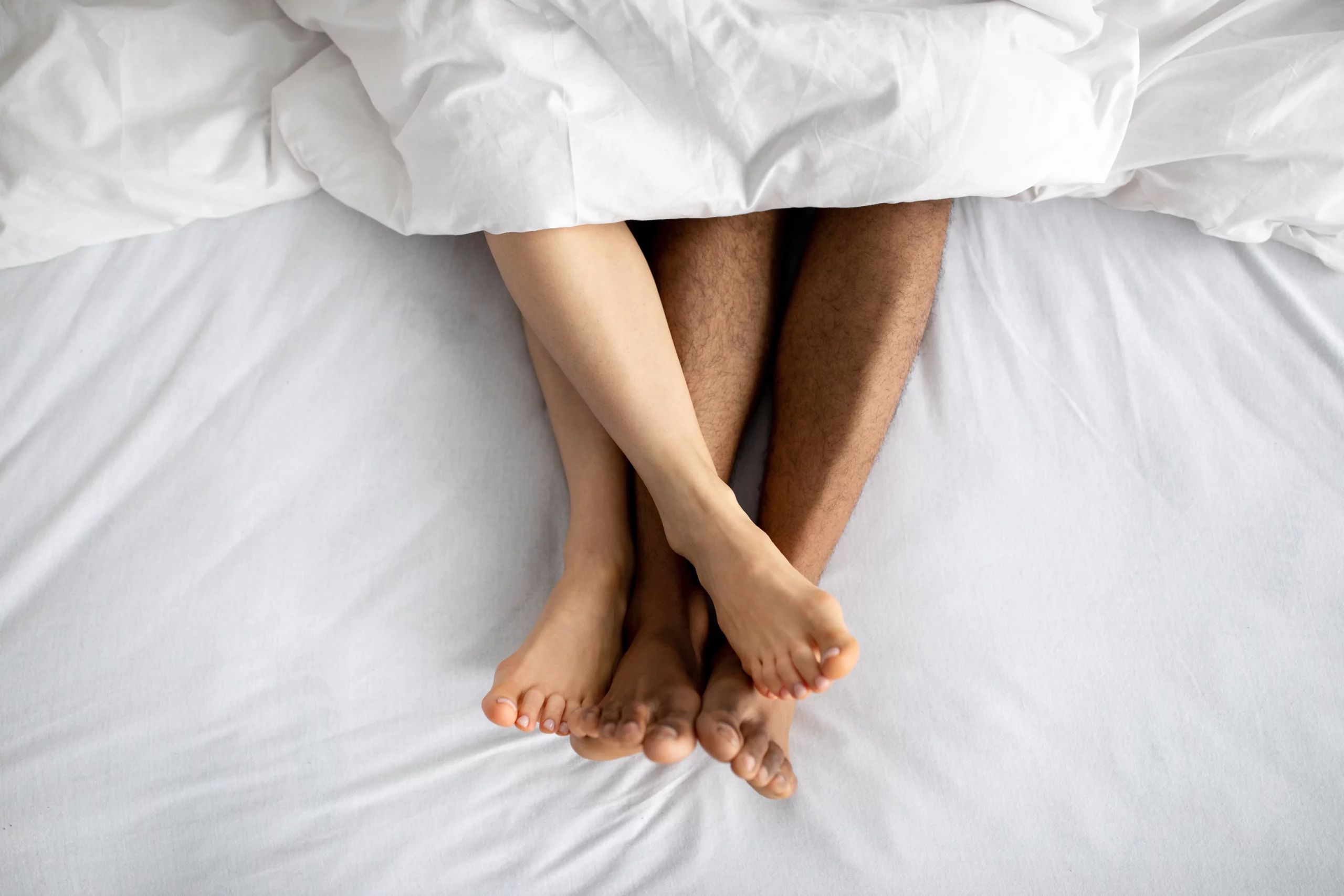 vista desde arriba de una cama con sabanas blancas y los pies desnudos y entrelazados de una pareja