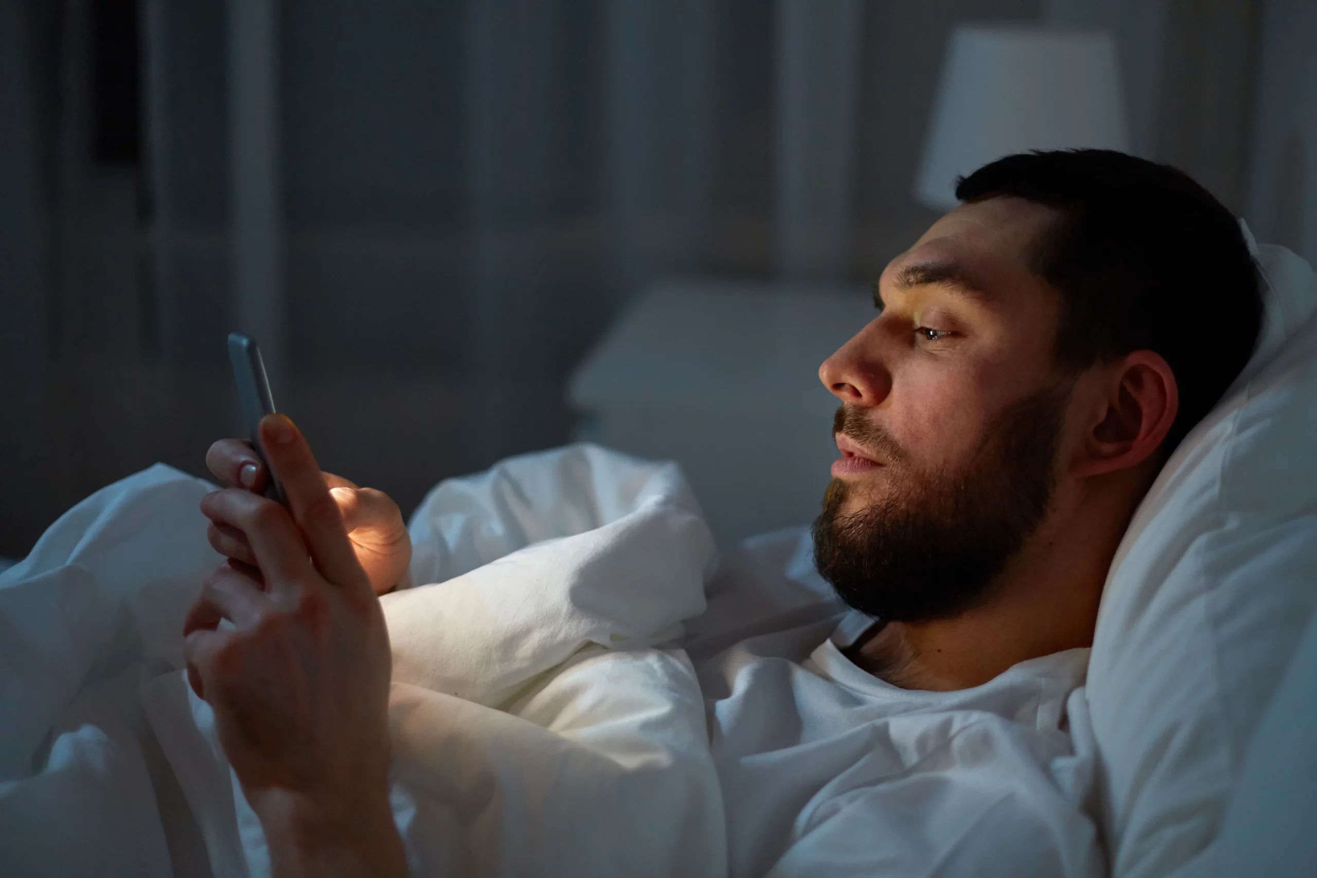 man scrolling through his phone in the bed at night